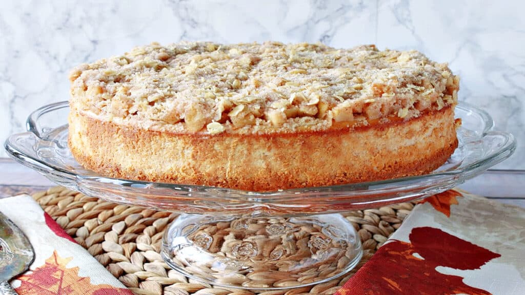 A whole Dutch Apple Cheesecake on a glass cake stand.