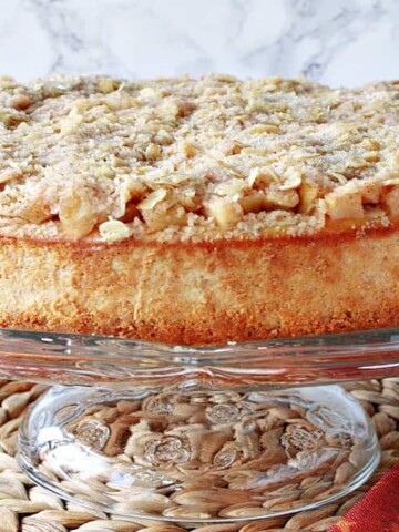 A whole Dutch Apple Cheesecake on a glass cake stand.