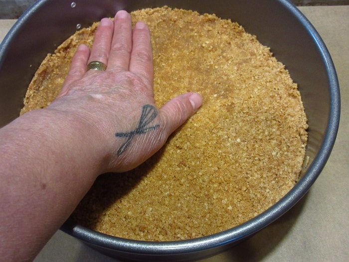 A hand pressing crumbs for a cheesecake crust.