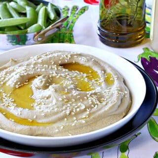 A white bowl filled with Eggplant and Chickpeas Hummus in the foreground and a small bowl of sugar snap peas in the background.