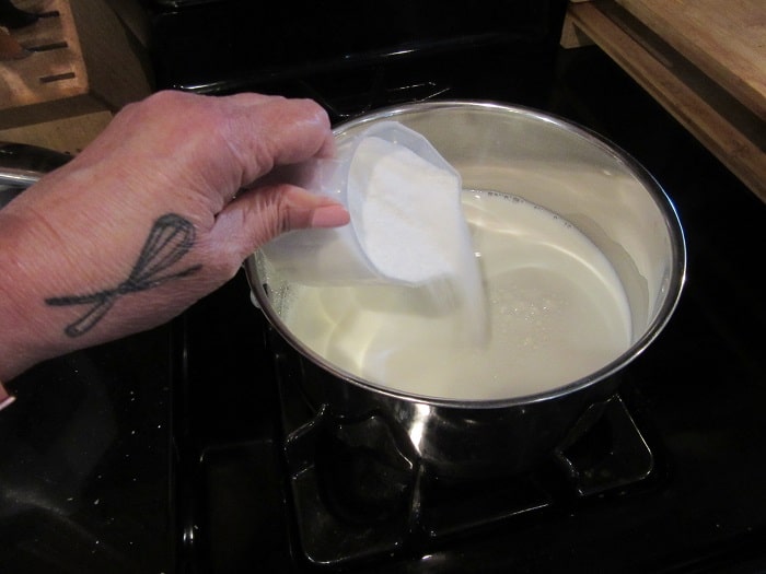 Sugar being added to milk in a suacepan.