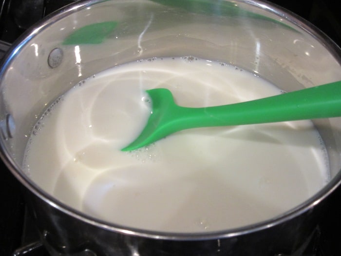 A green silicone spatula in a saucepan with milk and sugar.