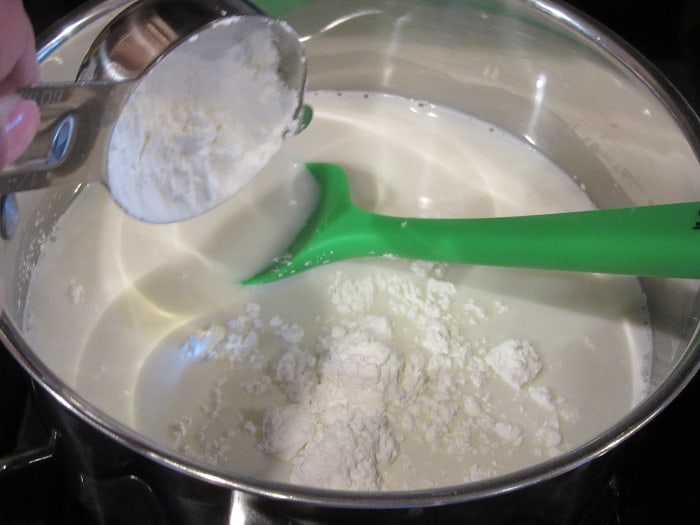 Flour being added to a saucepan with milk.