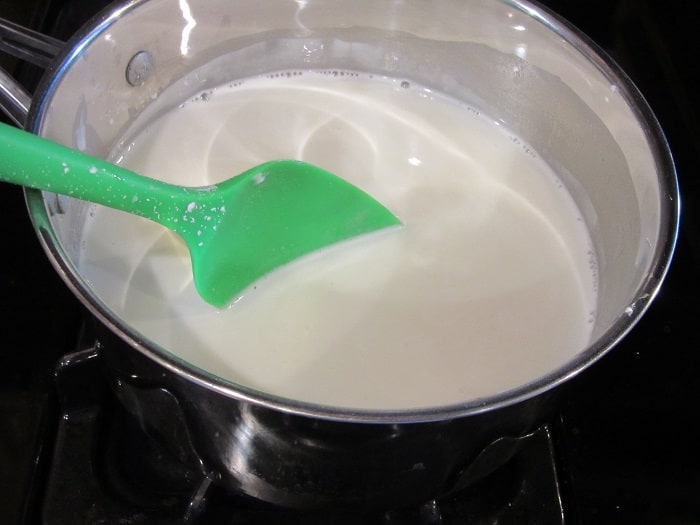 A green silicone spatula in a saucepan with milk.