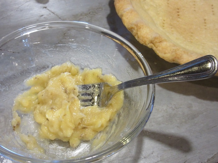 Mashed bananas in a glass bowl with a fork.