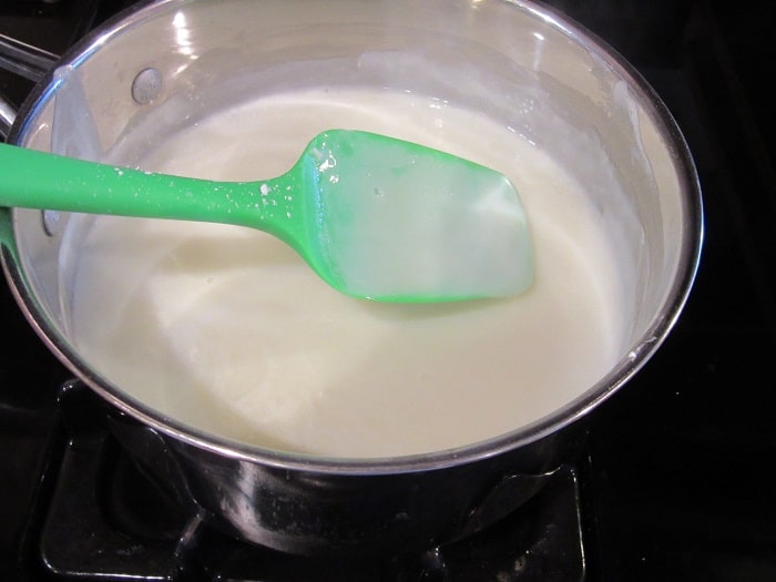 A thickening sauce in a saucepan with a green spatula.