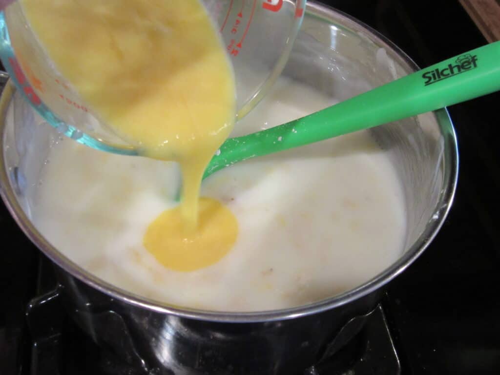 Tempered eggs being added to a saucepan for making banana cream pie.