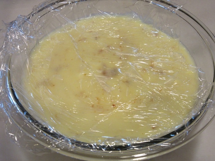The custard for a banana cream pie in a glass bowl with plastic wrap on top. 