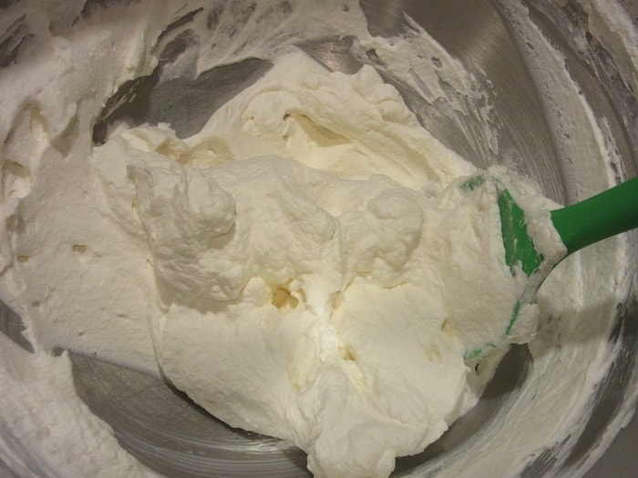 Homemade whipped cream in a bowl with a green silicone spatula.