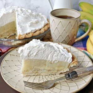 A slice of Banana Cream Pie on a cream colored plate with a fork.