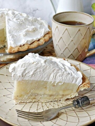 A slice of Banana Cream Pie on a cream colored plate with a fork.