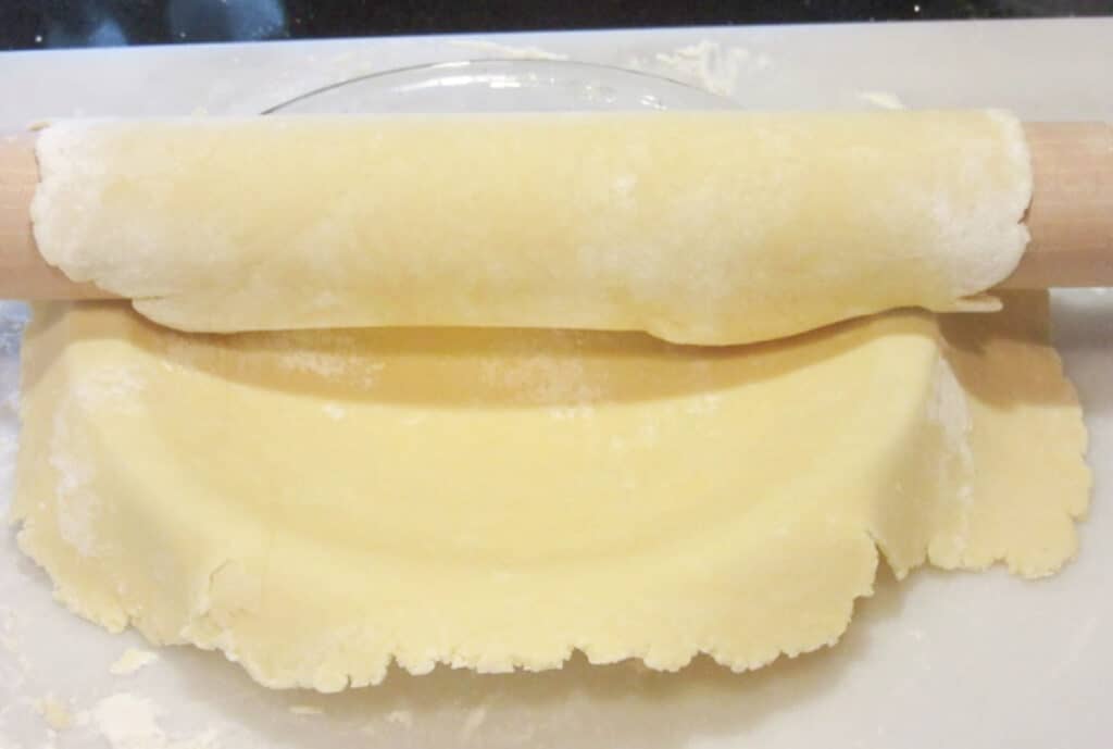 Mom's Homemade Pie Crust rolled onto a rolling pin and transferred to a waiting pie plate.