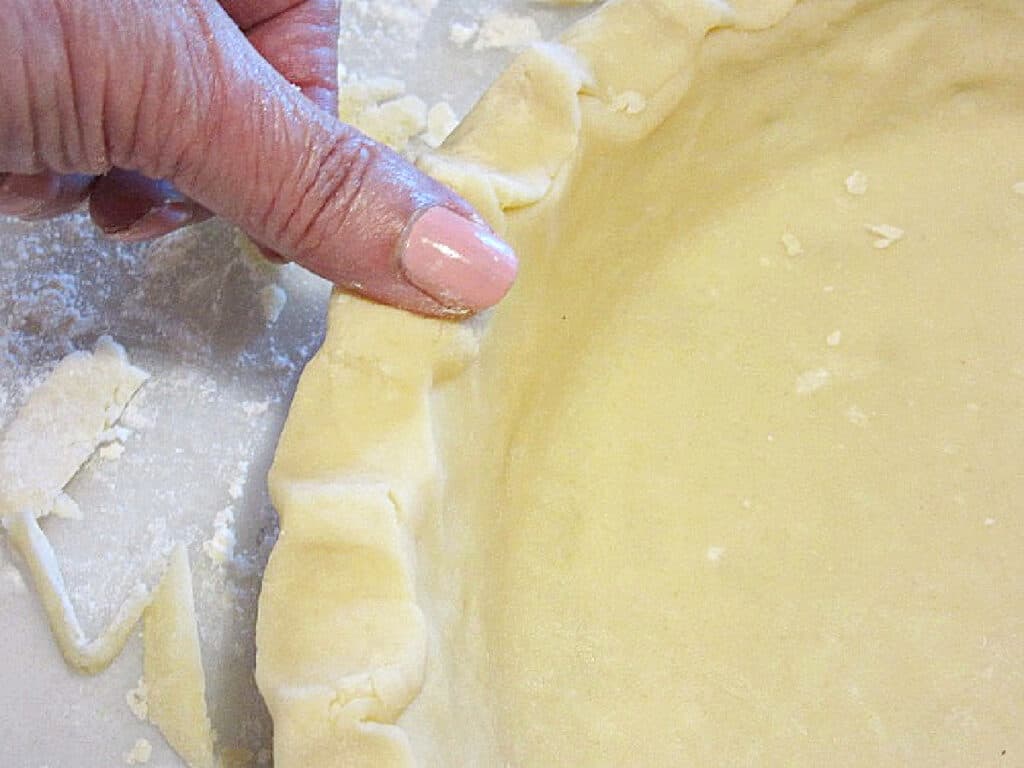 A closeup horizontal photo of a hand forming a decorative pie crust edge with homemade pie crust.