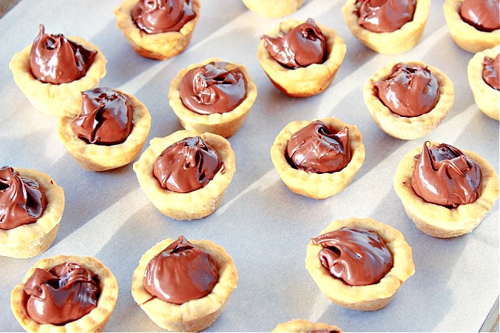 A bunch of Nutella Cookie Cups on a white sheet of parchment paper with sunlight and shadows.