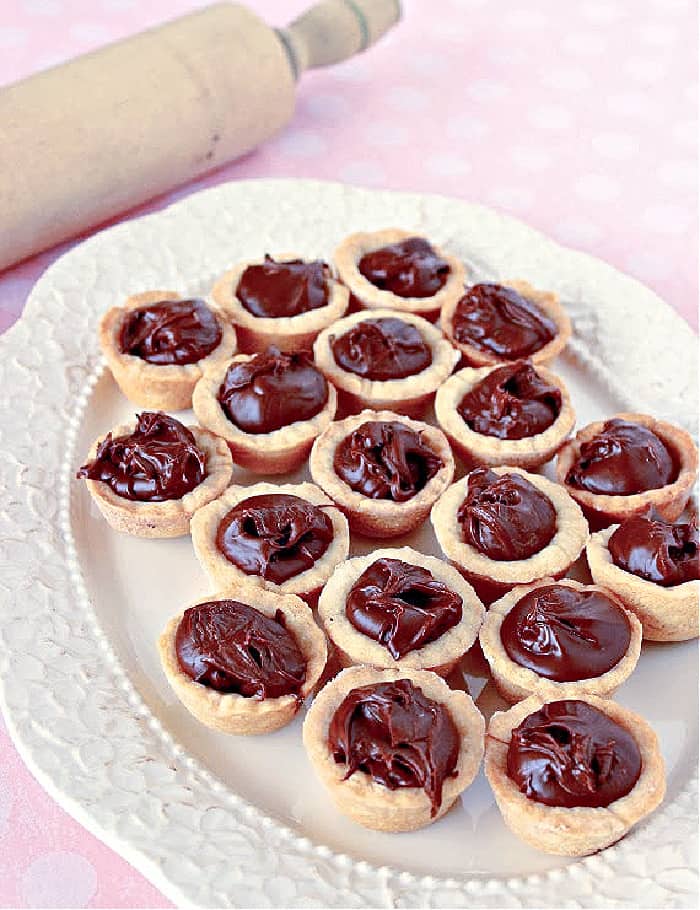 A pretty white platter filled with Nutella Cookie Cups on a pink polka dot tablecloth. 