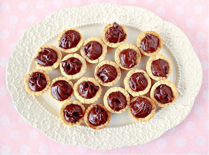 A direct overhead horizontal photo of Nutella Cookie Cups on a pretty white platter with a pink and white polka dot tablecloth.