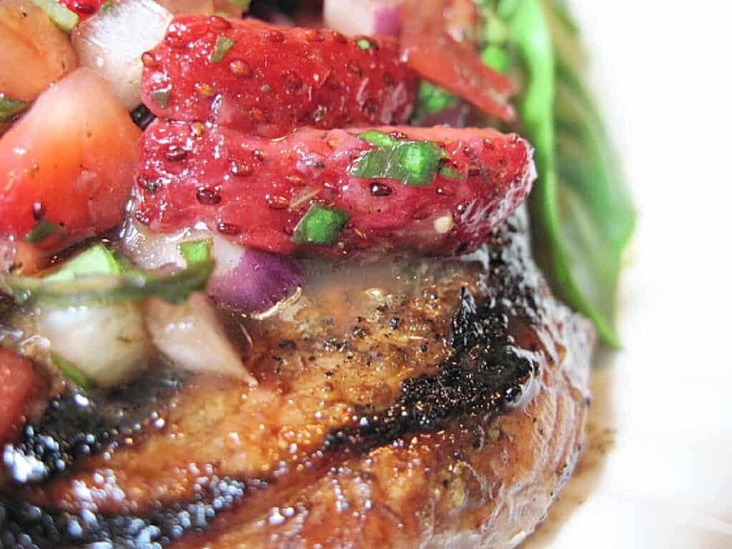 A super closeup photo of a cooked pork chop topped with strawberry relish with basil and red onion.