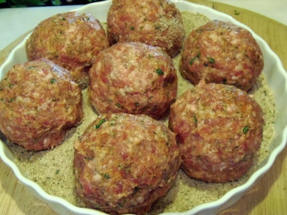 Uncooked Scotch Eggs in a tray with breadcrumbs. 