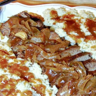 A Slow Cooker Beef Brisket on a white plate covered in gravy and onions.