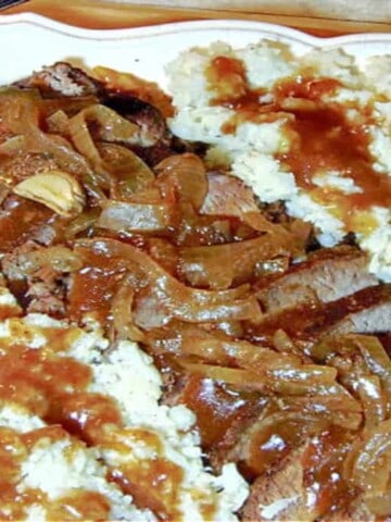 A Slow Cooker Beef Brisket on a white plate covered in gravy and onions.