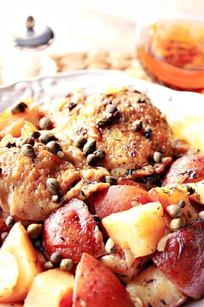 A vertical closeup image of a pile of Vesuvio potatoes with chicken, capers and thyme.