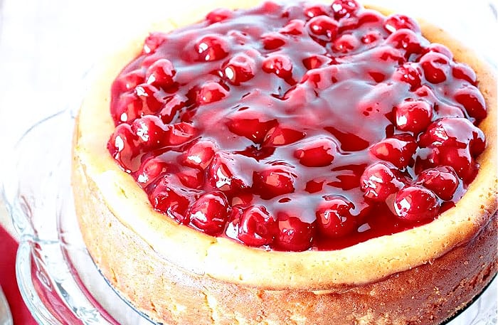 A very close photo of a Traditional Cherry Cheesecake with glistening red cherry pie filling on top.