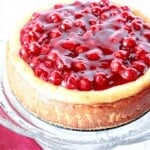 A baked cherry cheesecake on a glass cake stand.