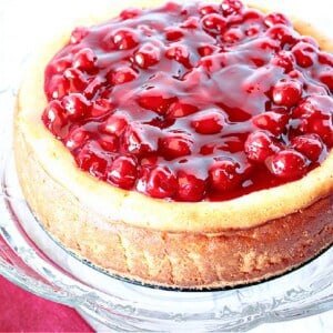 A baked cherry cheesecake on a glass cake stand.