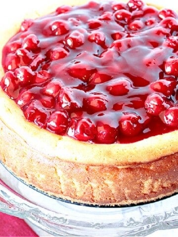 A baked cherry cheesecake on a glass cake stand.