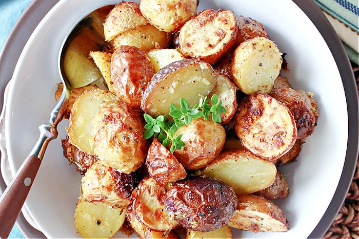 Direct overhead photo of a white bowl filled with golden air fryer mini potatoes with fresh thyme leaves for garnish.