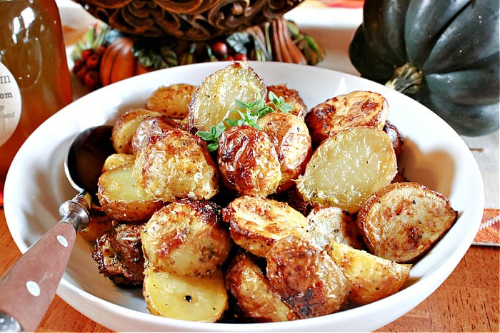 A closeup horizontal photo of a white bowl and a spoon along with golden Air Fryer Baby Potatoes and some fresh thyme as garnish.