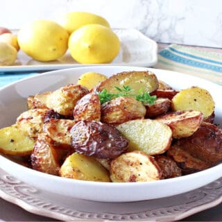 A horizontal photo of a white bowl filled with Air Fryer Baby Potatoes with fresh lemons and potatoes in the background.