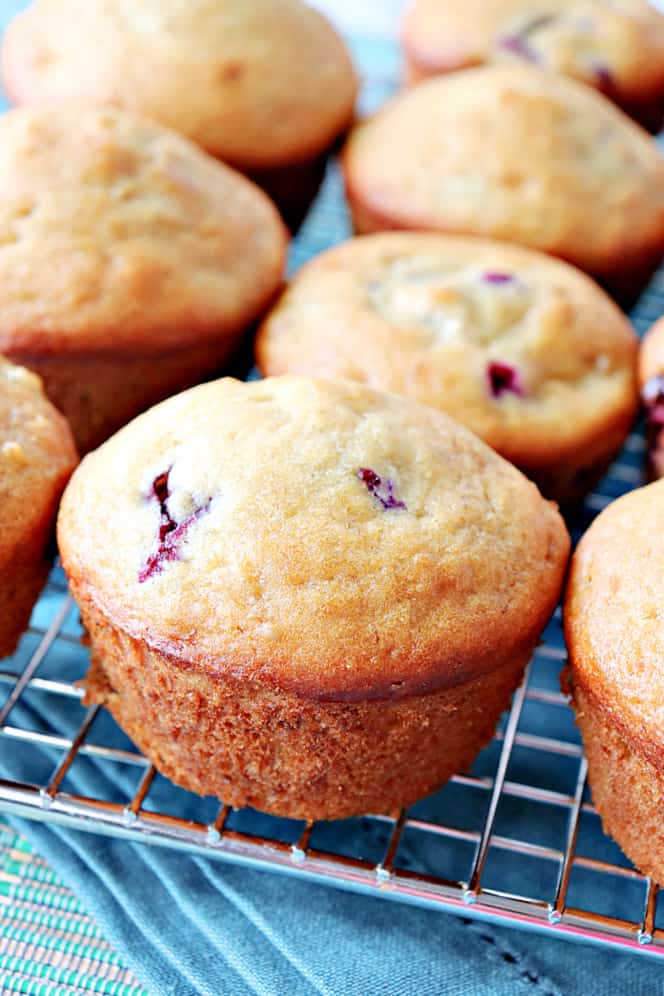 A closeup vertical photo of breakfast muffins with blueberry and banana flavor with a cooling rack and a blue napkin.