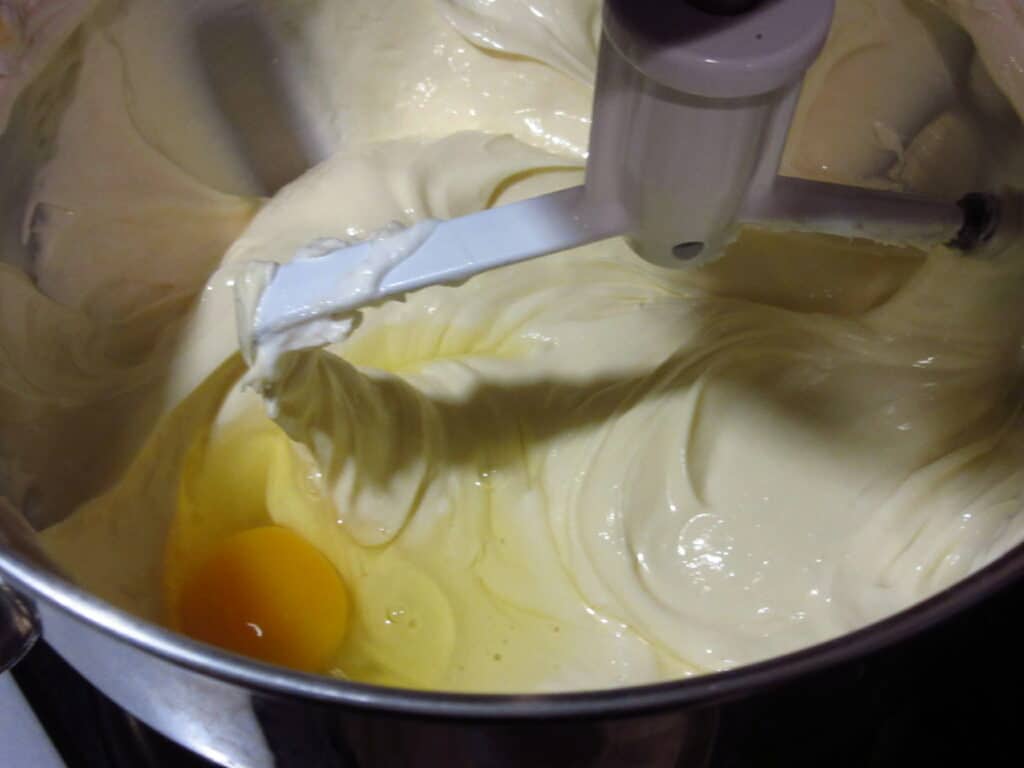An egg in a bowl with cheesecake mixture.
