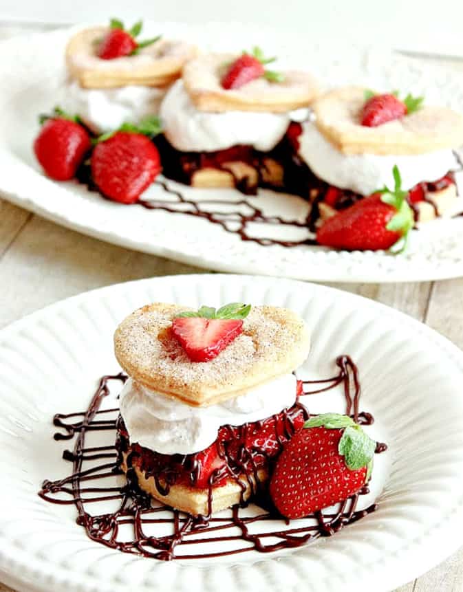 A vertical closeup photo of one strawberry pie tower using crust-pie hearts with a tray of three in the background.