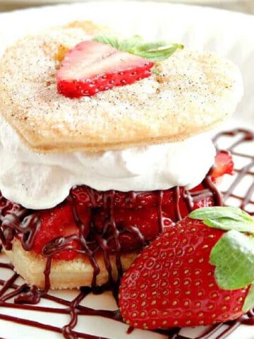 A Deconstructed Strawberry Pie on a white plate with whipped cream and a chocolate drizzle.