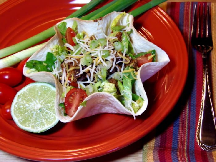 A Lighter Taco Salad is in a tortilla bowl and on a red plate with a lime and scallions.