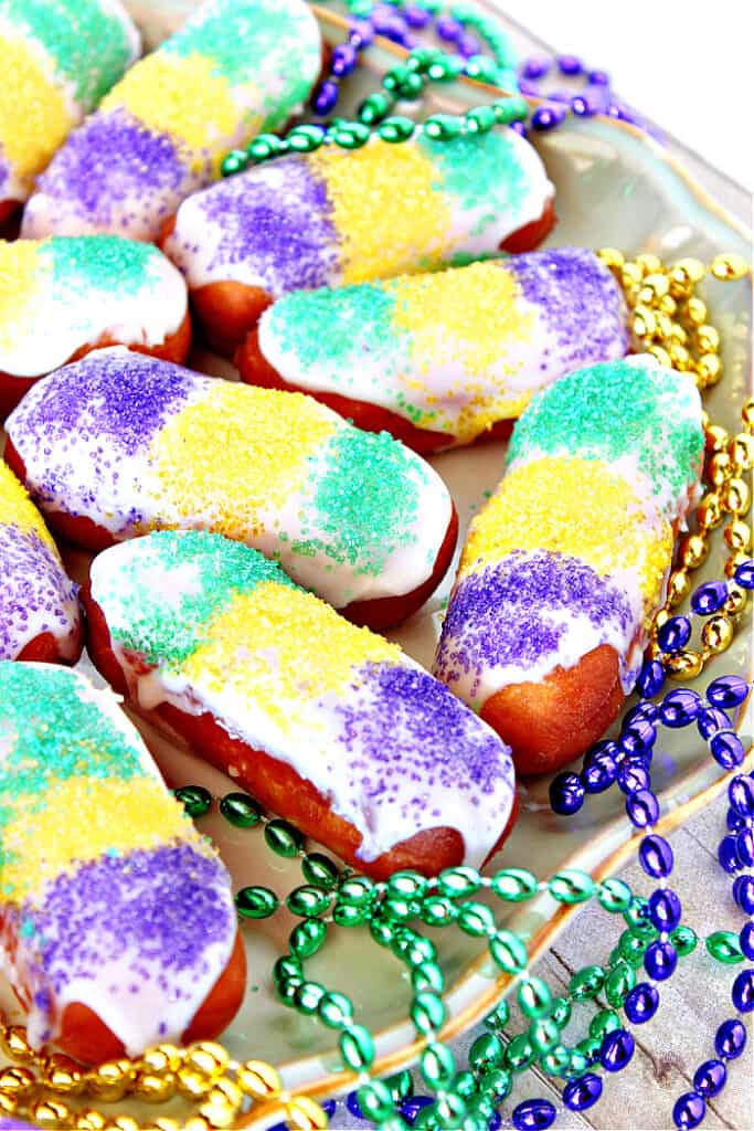 A vertical closeup of a plate of Mini Long Johns along with purple, green, and yellow sanding sugars.