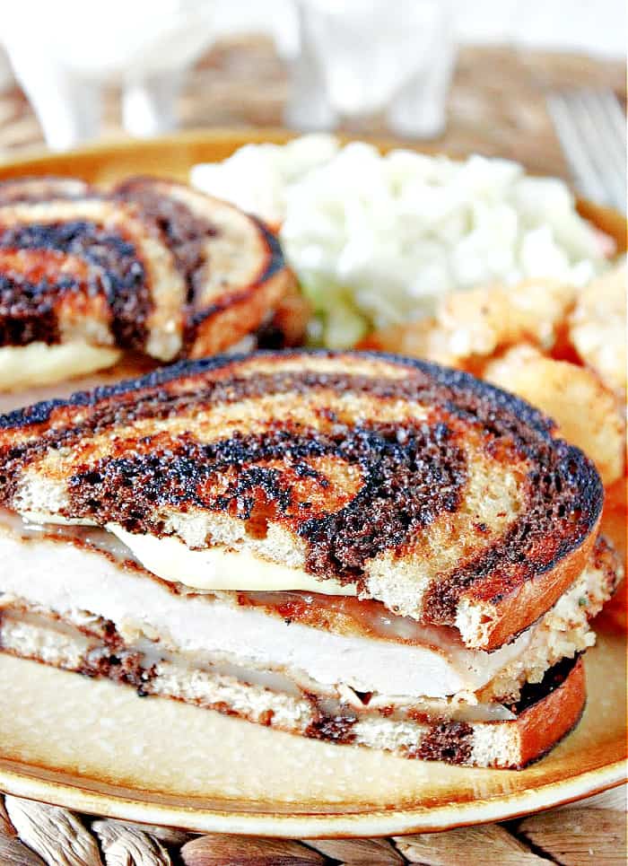 A vertical closeup photo of a Schnitzel Melt Sandwich on marbled rye bread and honey mustard mayonnaise.
