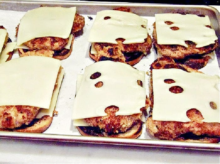 A baking sheet filled with open-faced Schnitzel Melt Sandwiches with Swiss cheese on top.