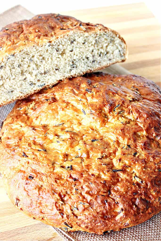 A vertical closeup of a golden rustic loaf of Wild Rice Bread with Onions along with a sliced loaf on top.