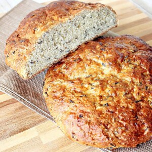 Two golden loaves of Wild Rice Bread on a cooling rack with one cut in half.