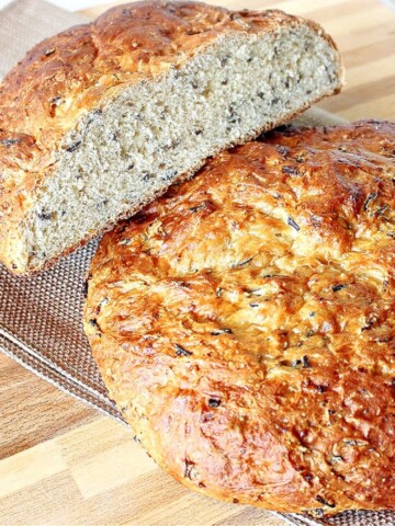 Two golden loaves of Wild Rice Bread on a cooling rack with one cut in half.