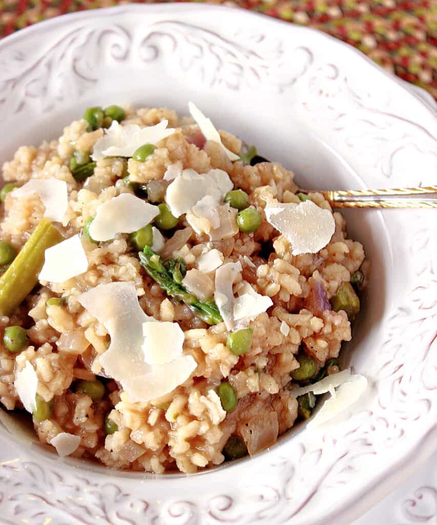 A vertical overhead closeup of a bowl of Asparagus and Pea Risotto garnished with shards of Parmesan cheese.