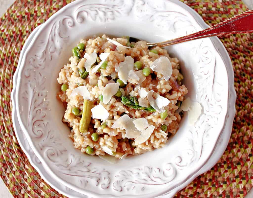 A direct overhead photo of a white bowl filled with Asparagus and Pea Risotto along with a spoon and a placemat.