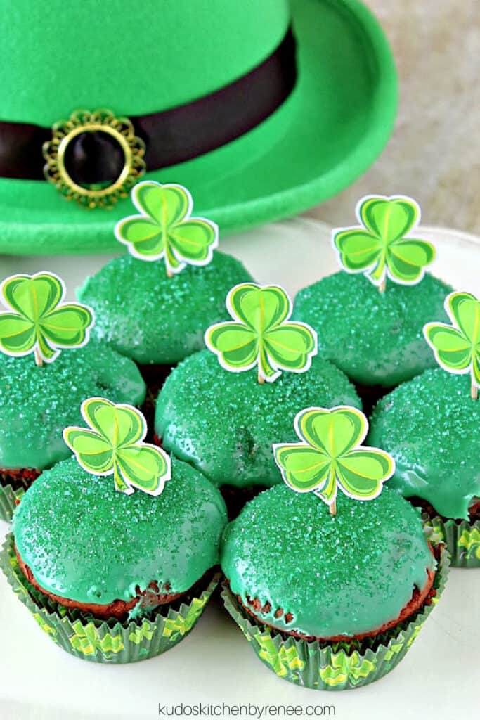A vertical closeup photo of cute green Chocolate Mint Brownie Cupcakes with sanding sugar and paper shamrocks on top.