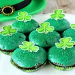 A white scalloped plate filled with Chocolate Mint Brownie Cupcakes with a green glaze and paper shamrocks on top.