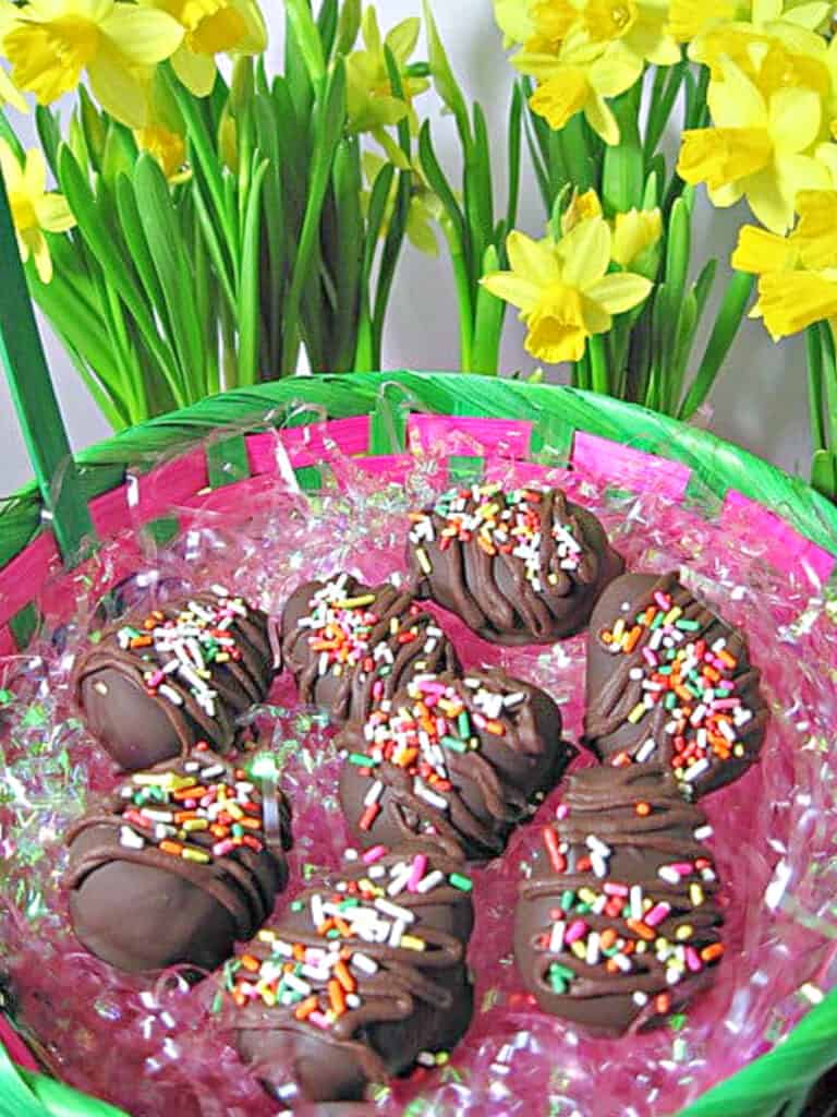 An Easter basket filled with Chocolate Peanut Butter Eggs in pink Easter glass with daffodils in the background.