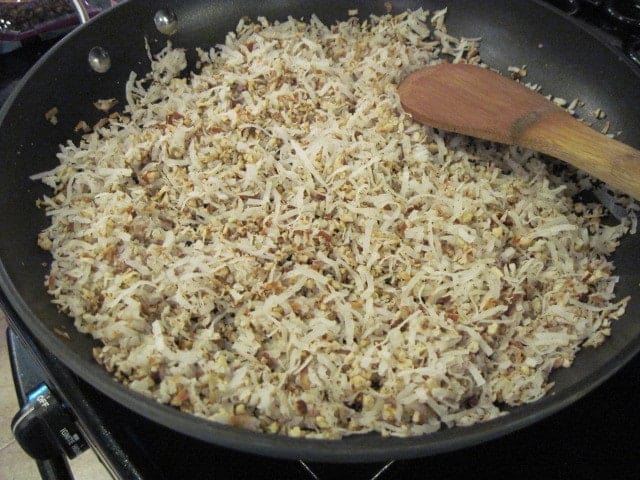 Coconut and chopped pecans in a skillet with a wooden spoon.
