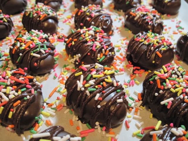 A closeup horizontal photo of colorful sprinkles on top of Chocolate Peanut Butter Eggs on parchment paper.